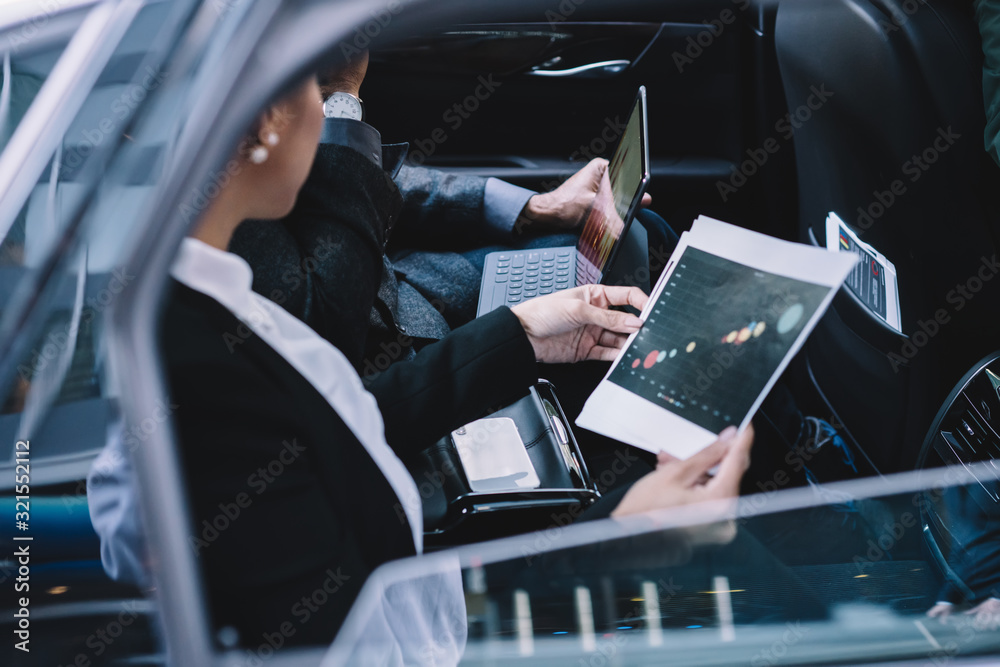 Diverse coworkers using digital tablet while examining reports in car Diverse coworkers using digital tablet while examining reports in car