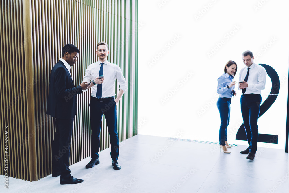 Fototapeta premium Multiracial coworkers using smartphones at office hall