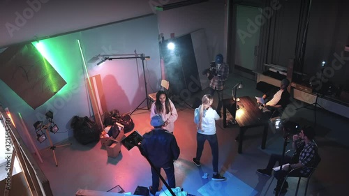 Bird's-eye shot of film shooting in a big film studio. Film crew working on movie production. Producer assistant gives action with movie clapper board and the film crew starting working.