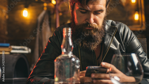 Lifestyle of modern businessman. Handsome bearded businessman is drinking expensive whiskey. Macho man scrolling news feed in his smartphone.