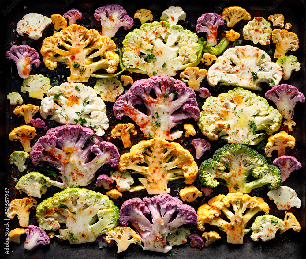 Sliced colorful cauliflowers seasoned with salt, herbs and spices and olive oil prepared for baking on a black background, top view. Healthy vegan food
