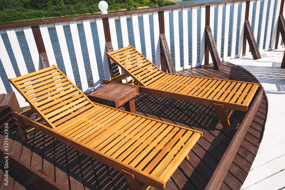 Stylish wooden sunbeds on the terrace of the landing stage. Outdoor recreation. River on the background. Stylish wooden sunbeds on the terrace of the landing stage. Outdoor recreation. River on the background.