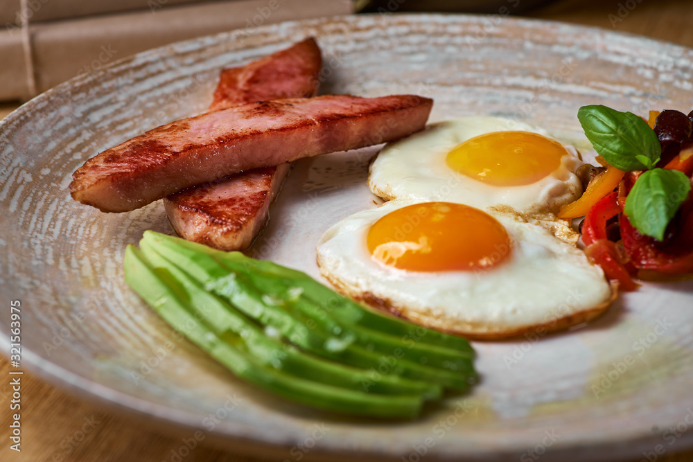 plate of fried eggs with bacon and avocad on wooden table. English breakfast on table