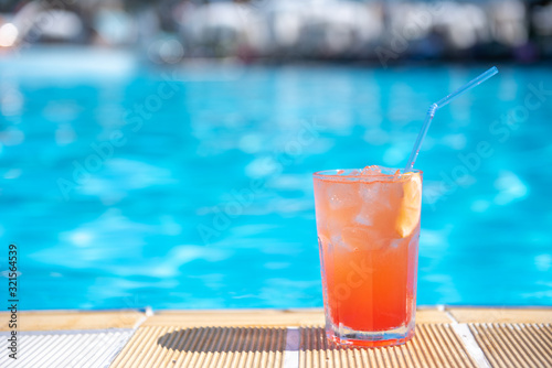 Fresh alcoholic red cocktail sex on beach with ice in glass on edge of pool in summer weather against background washed up pool and recreation area. Concept good holiday and travel, place for text.