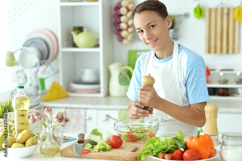 Cute boy preparing salad on kitchen table at home