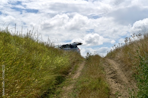 The dirt road leading up to the car is partially visible with an open raised trunk on a hill among the steppe grasses. photo