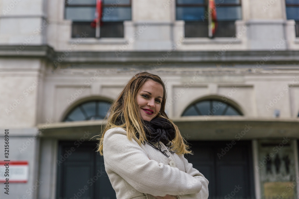 Fototapeta premium Business woman with white coat and black scarf poses smiling in front of an old city