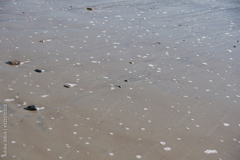 Small rocks and pebbles in the wet beach sand where the ocean water is flowing back after an incoming wave Small rocks and pebbles in the wet beach sand where the ocean water is flowing back after an incoming wave