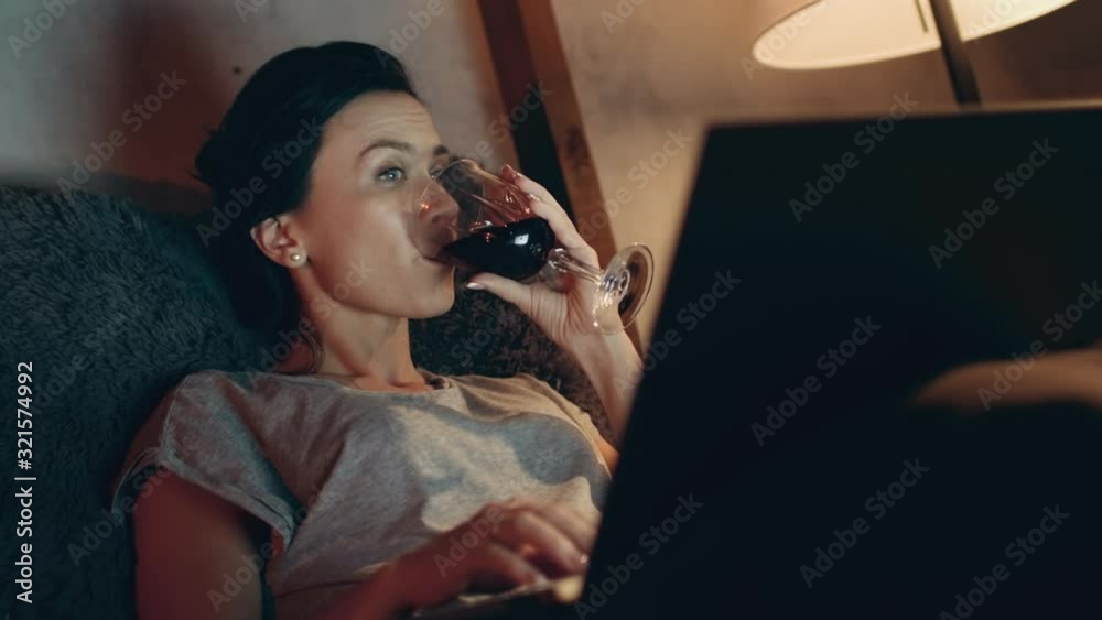 Woman drinking red wine with laptop. Girl surfing internet on computer.