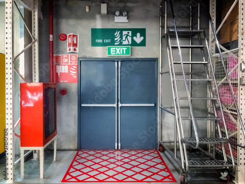 Fire exit emergency door red color metal material with alarm for safety protection  and white wall in building.Building Emergency Exit with Exit Sign and Fire Extinguisher.