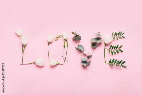 Word LOVE made of flowers and leaves on pink background.