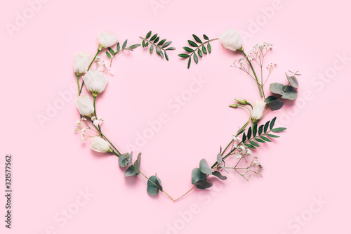 Heart symbol made of flowers and leaves on pink background.