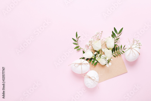 White Easter eggs and envelope with flowers and green leaves on pink background