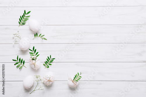 White Easter eggs with flowers and green leaves on white wooden background