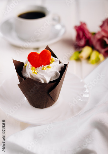Valentines day cupcake. Cupcake with white cream and red sugar hearts on a red background, bokeh effect, save space. St. Valentine's Day card