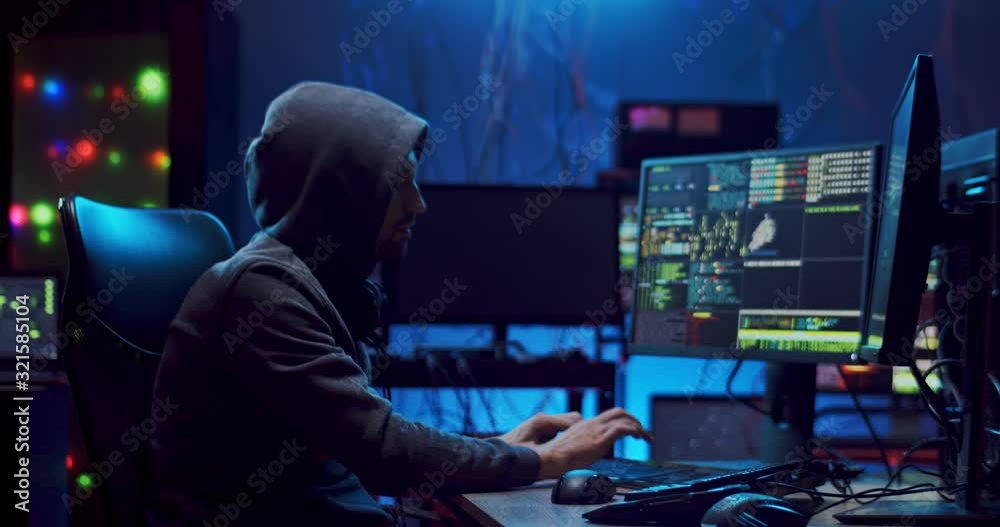 Young Caucasian man software developer working at night on two computers simultaneously and programming virus or antivirus.