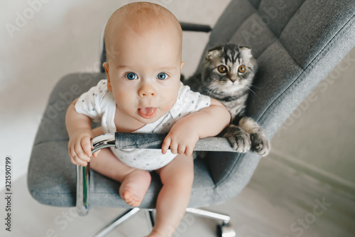 Obraz na płótnie Blonde baby boy with kitten is sitting on the chair and look to camera. Top view w salonie