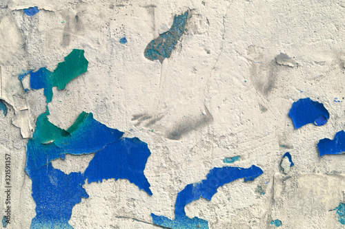 old weather-aged wall with crumbling plaster blue and green colors and scraps of paper on it © Oleg