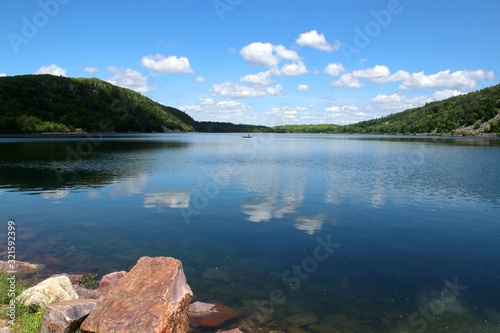Fototapeta Naklejka Na Ścianę i Meble -  Beautiful Wisconsin late spring nature background. Devil's Lake State Park landscape with view on the North shore and a lake water with cloudy blue sky reflection. Baraboo, WI, Midwest USA.