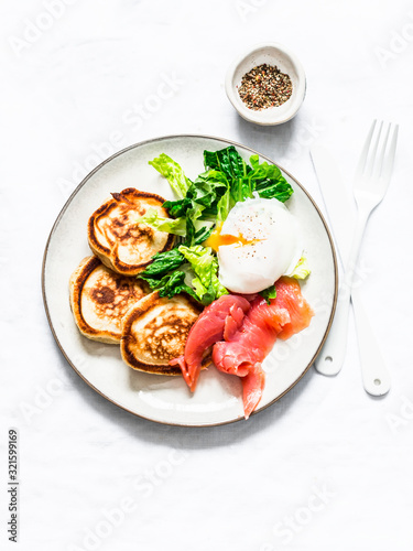Delicious healthy brunch - poached egg, smoked salmon, green salad and savory pancakes on a light background, top view