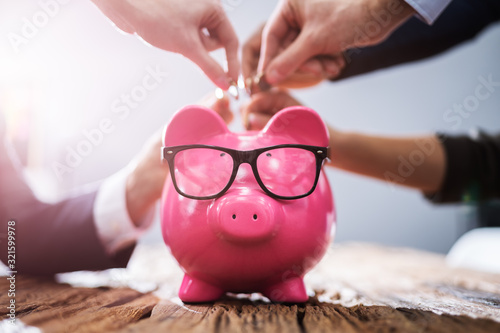 Crowdfunding Concept. People Inserting Coins Into Piggybank photo