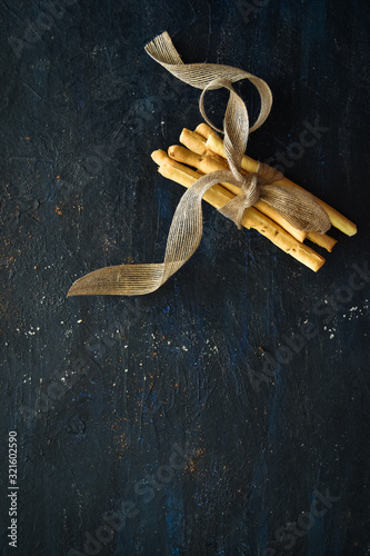 Bunch of grissini breadsticks tied together with a ribbon on dark background, breadsticks top view, italian breadsticks. Homemade, baked, soup, italian, restaurant, bakery concepts. copy space. photo