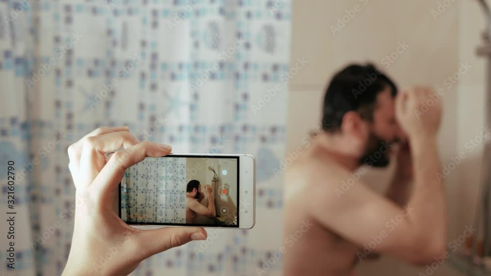 Happiness funny man washes in shower and dances, sings. Female hand holds phone and shots video of how husband is washing. Slow Motion