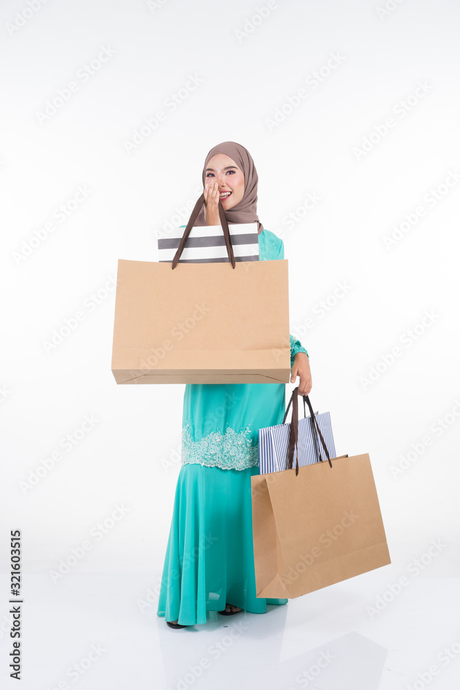 A beautiful and excited Muslim female model in a Asian traditional dress modern kurung carrying shopping bags isolated on white background. Eidul fitri festive preparation shopping concept A beautiful and excited Muslim female model in a Asian traditional dress modern kurung carrying shopping bags isolated on white background. Eidul fitri festive preparation shopping concept