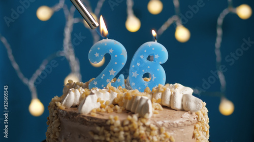 Birthday cake with 26 number candle on blue backgraund set on fire by lighter. Close-up photo