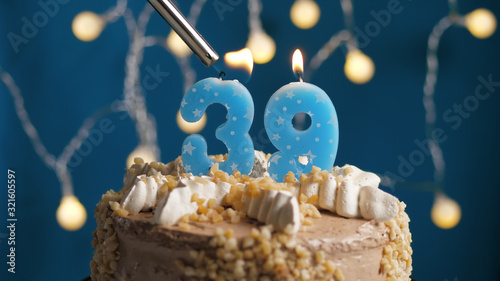 Birthday cake with 39 number candle on blue backgraund set on fire by lighter. Close-up photo