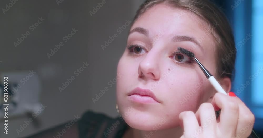 Beautiful young blond woman putting make up on her eyes through a mirror. She is applying mascara on her left eye eyelashes. High dynamic range professional footage. Beautiful young blond woman putting make up on her eyes through a mirror. She is applying mascara on her left eye eyelashes. High dynamic range professional footage.
