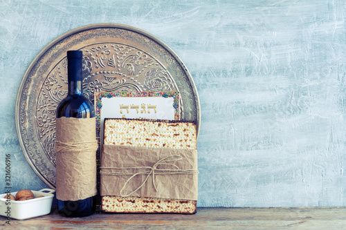 Metal plate with matzah or matza and Passover Haggadah on a vintage wood background presented as a Passover seder feast or meal with copy space. Translation: Passover Haggadah