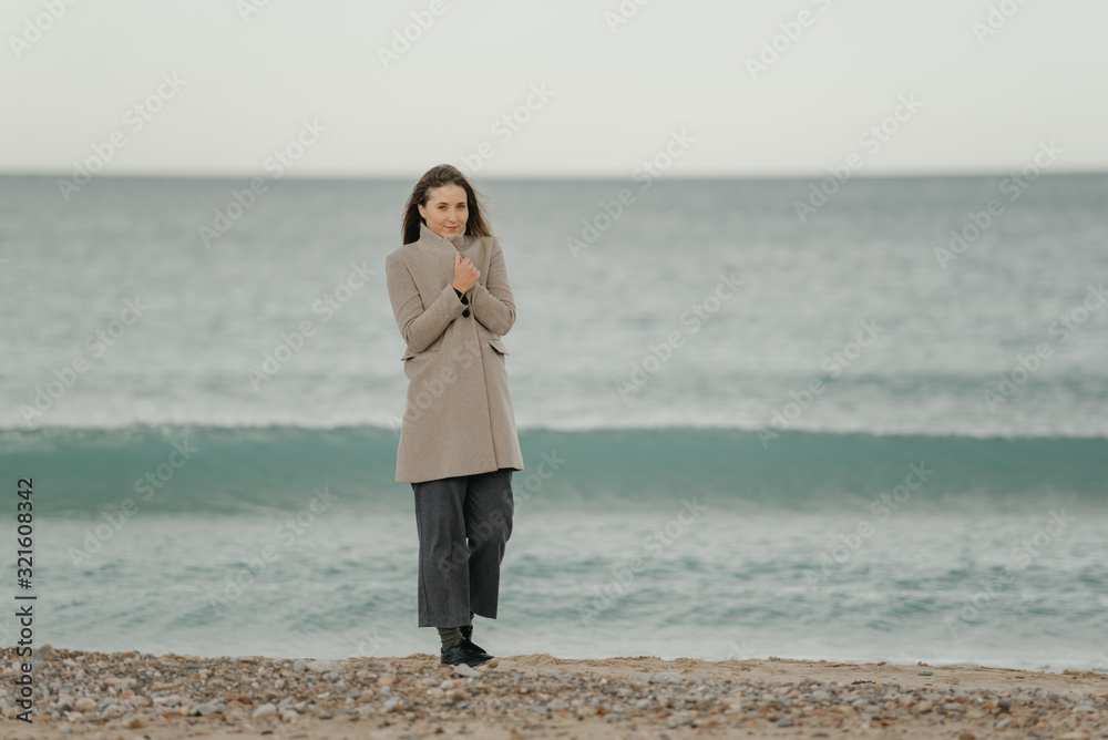 A gorgeous pretty woman with long hair wraps herself in a coat near the Mediterranean Sea A gorgeous pretty woman with long hair wraps herself in a coat near the Mediterranean Sea