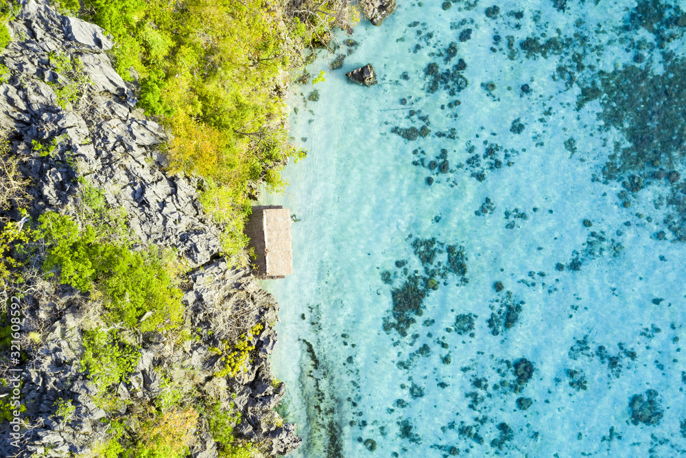 View from above, stunning aerial view of a bungalow surrounded by rocky cliffs bathed by a turquoise, crystal clear sea. Malwawey Coral Garden, Coron Island, Palawan, Philippines.