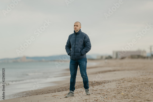 A muscular bald man in the jeans, bologna jacket and sneakers looks in the Mediterranean Sea