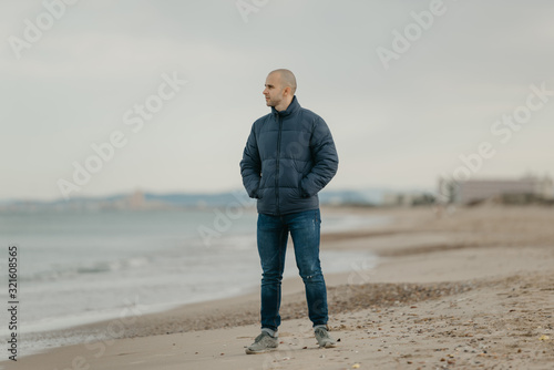 A muscular bald man in the jeans, bologna jacket, and sneakers looks in the Mediterranean Sea