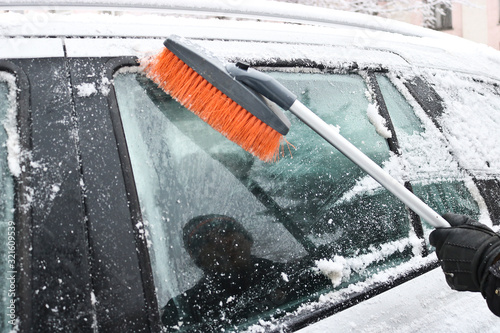 Man cleans the snow from a car with a brush. Winter car care.