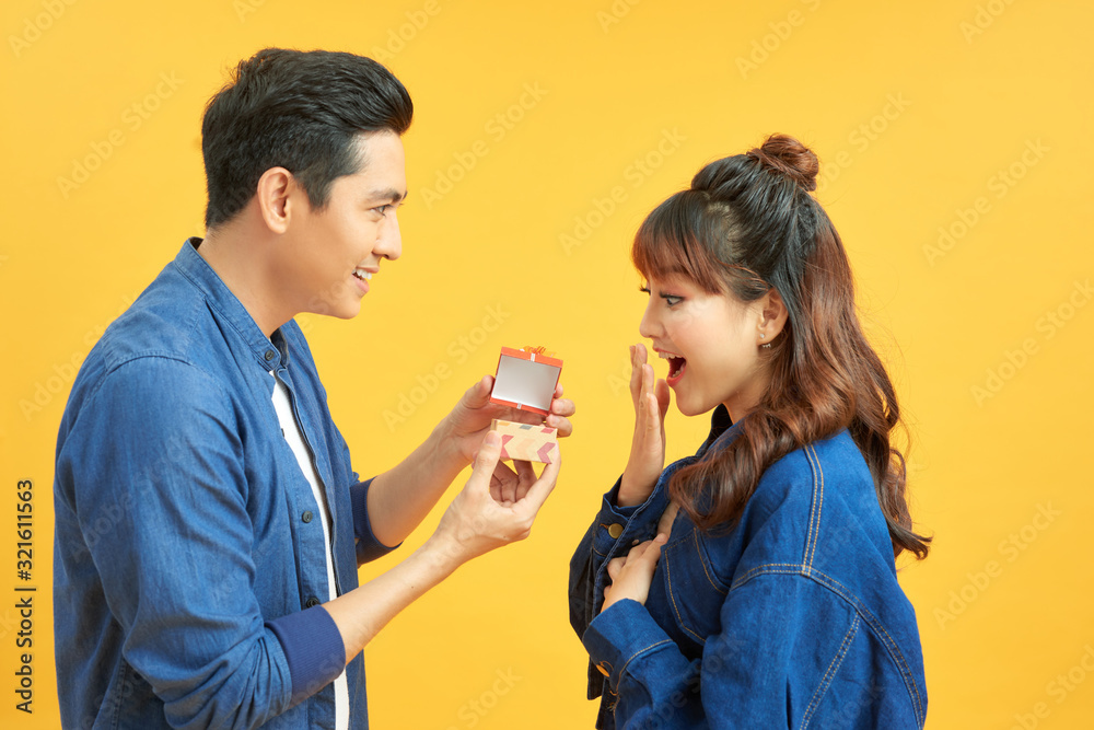 love, couple, proposal and people concept - man giving diamond engagement ring in little red box to happy woman over yellow background love, couple, proposal and people concept - man giving diamond engagement ring in little red box to happy woman over yellow background