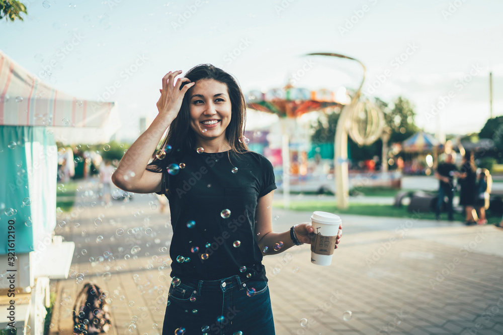 Fototapeta premium Attractive woman feeling happy emotions resting on vacation in amusement park, cheerful smiling hipster girl having fun with soap bubbles in air entertaining during summer vacation on city festival.