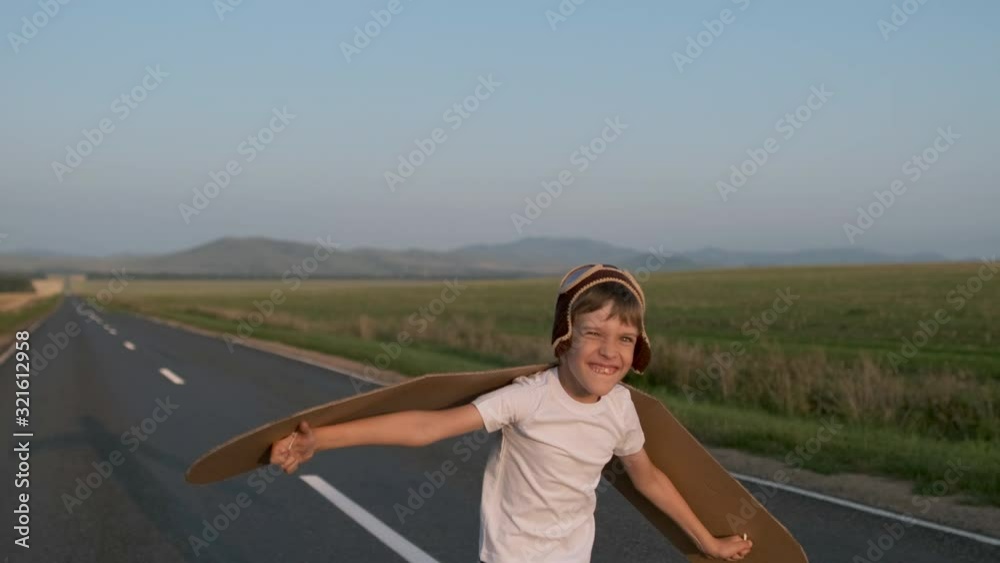 Happy smiling little boy child aviator pilot of airplane running with toy cardboard plane wings in road. Kid dreams of flying, traveling in summer nature at sunset outdoors, travel dream, 4 K slow-mo Happy smiling little boy child aviator pilot of airplane running with toy cardboard plane wings in road. Kid dreams of flying, traveling in summer nature at sunset outdoors, travel dream, 4 K slow-mo