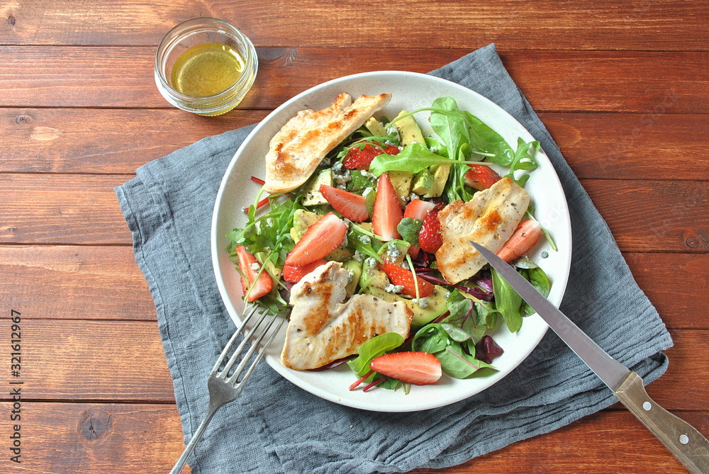 Chicken salad with avocado, strawberries, arugula, beet leaves and blue cheese Healthy food concept Avocado salad with chicken on wooden background