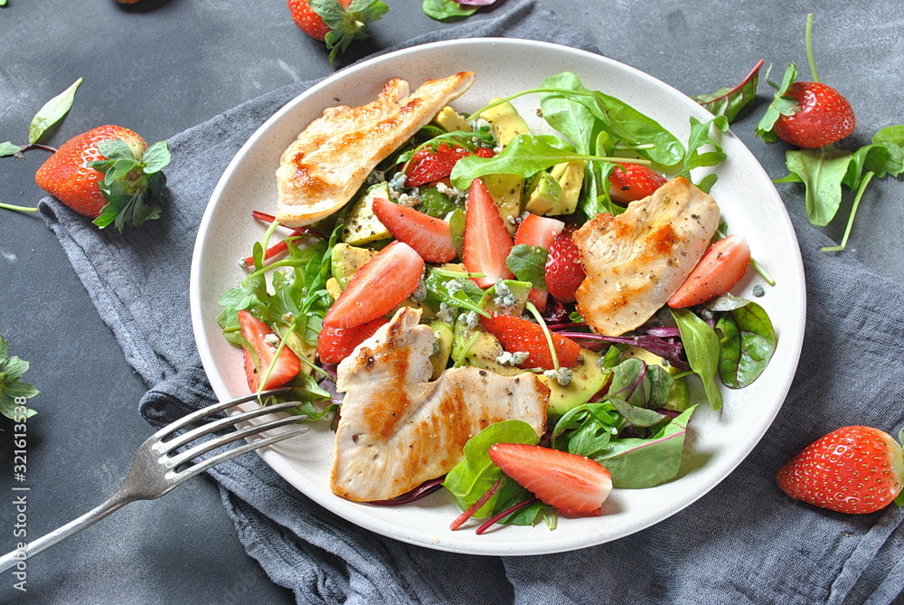 Chicken salad with avocado, strawberries,blue cheese, arugula, beet leaves. Healthy lunch avocado bowl, plate with chicken and strawberries on the dark gray background. Healthy food concept.