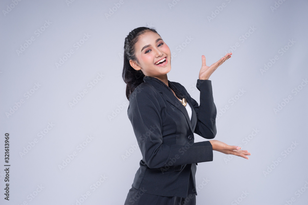 An attractive woman wearing business attire with gestures towards copyspace area isolated on grey. Good for manipulation works for technology, transportation, business or finance theme. An attractive woman wearing business attire with gestures towards copyspace area isolated on grey. Good for manipulation works for technology, transportation, business or finance theme.