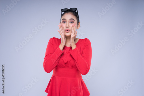 An attractive woman wearing casual red attire with gestures and poses towards copyspace isolated on grey. Good for technology, transportation, business or finance concept