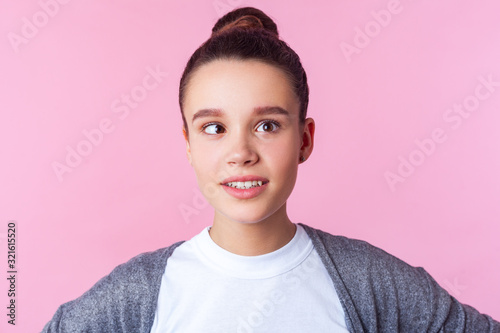 Portrait of adorable funny brunette teen girl with bun hairstyle in casual clothes fooling around with crossed eyes, having fun, childish positive face. indoor studio shot isolated on pink background photo
