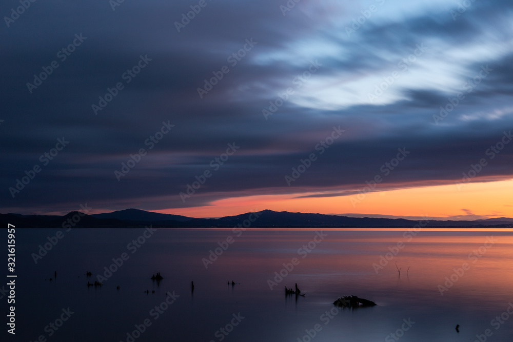 Naklejka premium Sunset a Trasimeno lake (Umbria, Italy), with fishing net poles and branches on perfectly still water