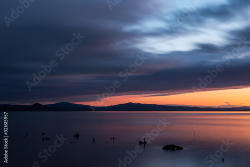 Sunset a Trasimeno lake (Umbria, Italy), with fishing net poles and branches on perfectly still water