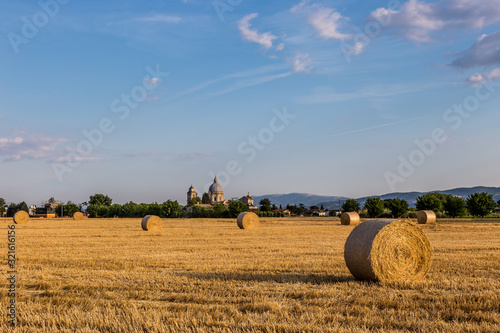 A field with haybales at golden hour, with the Santa Maria degli Angeli church (Assisi) in the background photo