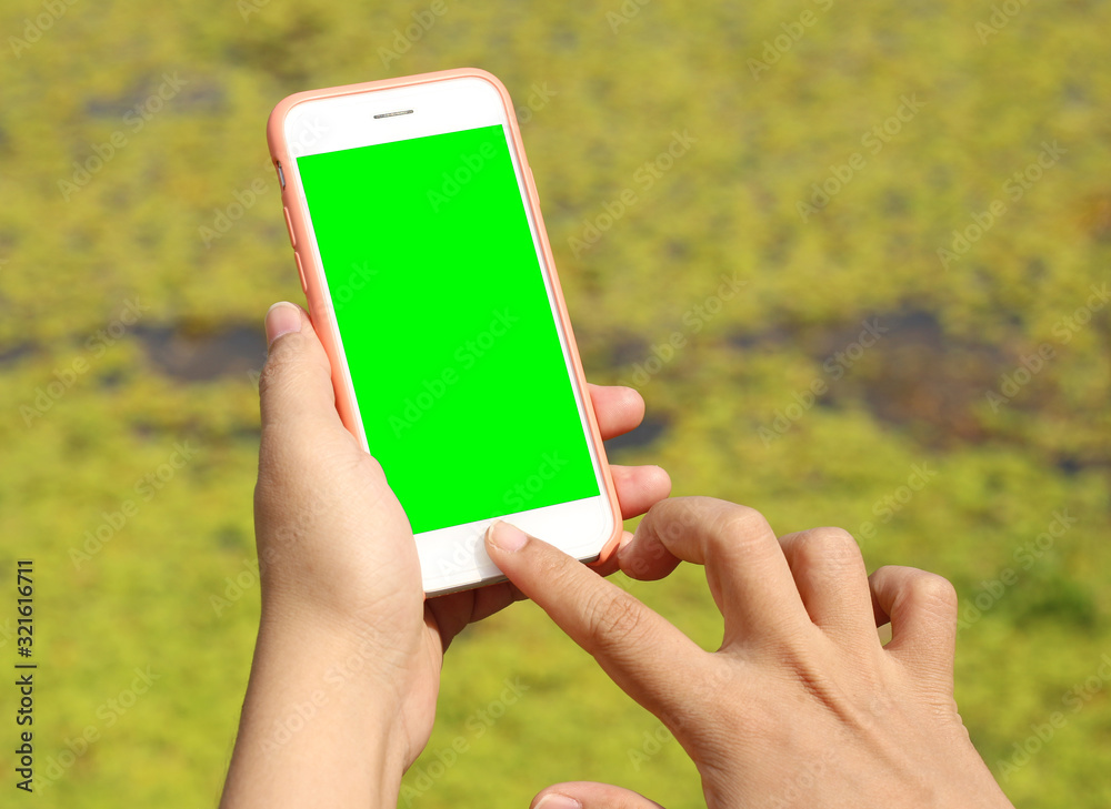 Hand woman holding mobile smart phone with blank green screen at park outdoor.