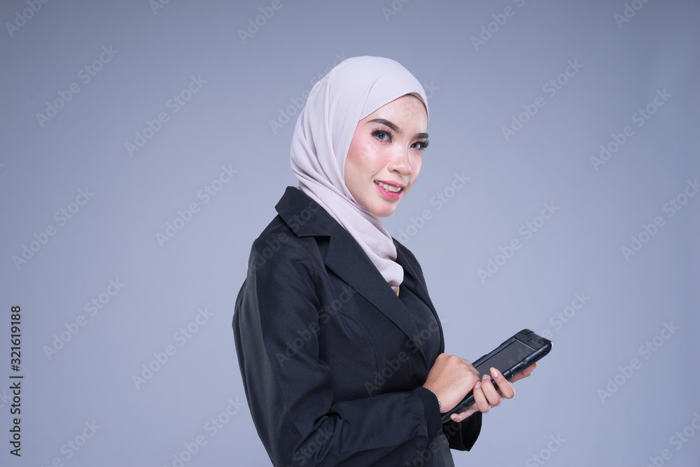 Half length portrait of an attractive Muslim businesswoman wearing hijab with tablet and gestures isolated on grey background. For image cutout for corporate, technology, business or finance.